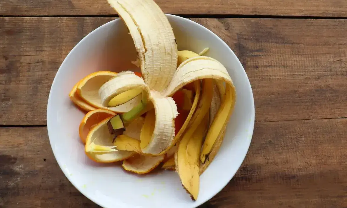 Skórki banana i pomarańczy w białej misce, gotowe na nawóz z banana dla roślin.